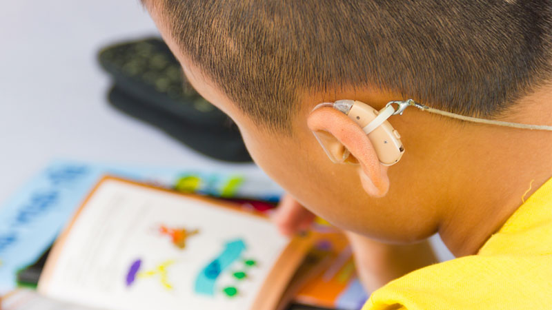 Child with hearing aids looking at a book